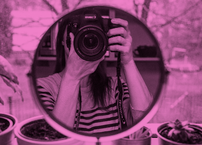  mirror shows a reflection woman holding a camera in front of her face