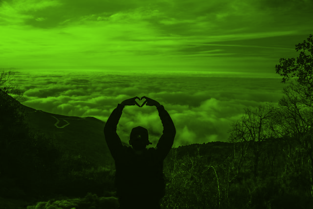 Man standing atop a hill holding up his hands in a heart sign