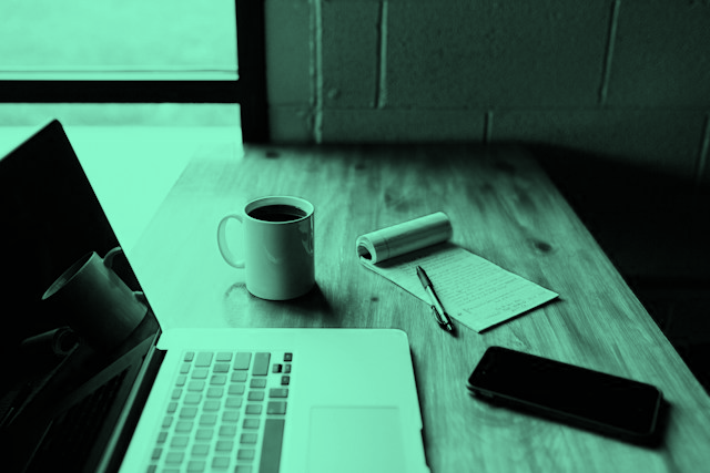 Image of a laptop, coffee mug, written notepad, and a phone on a work desk